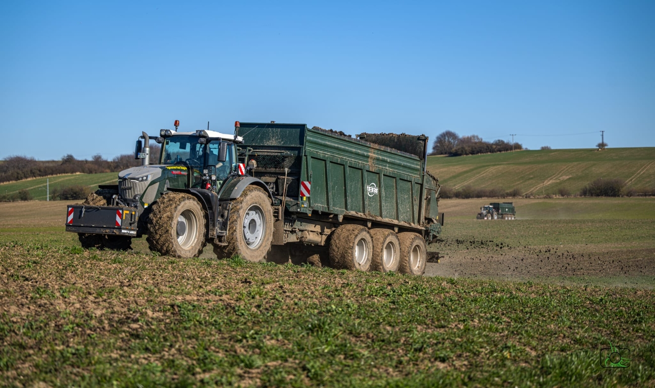 Ein Fendt 900 Vario fährt mit einem Mistbreiter auf einer Wiese, beide Produkte in der Farbe Tannengrün.