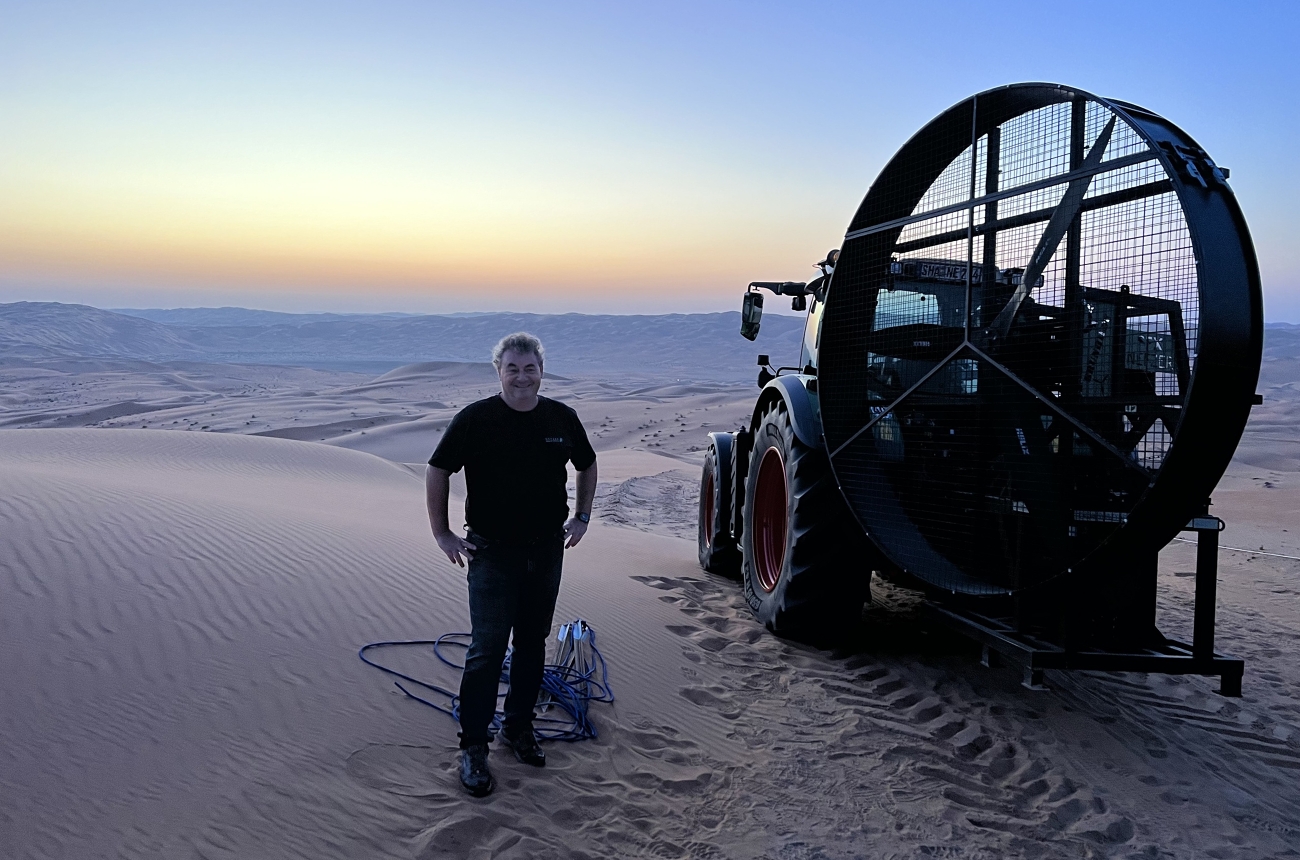 Ein Mann steht in der Wüste neben einem Fendt 900 Vario, der eine große Windmaschine antreibt.