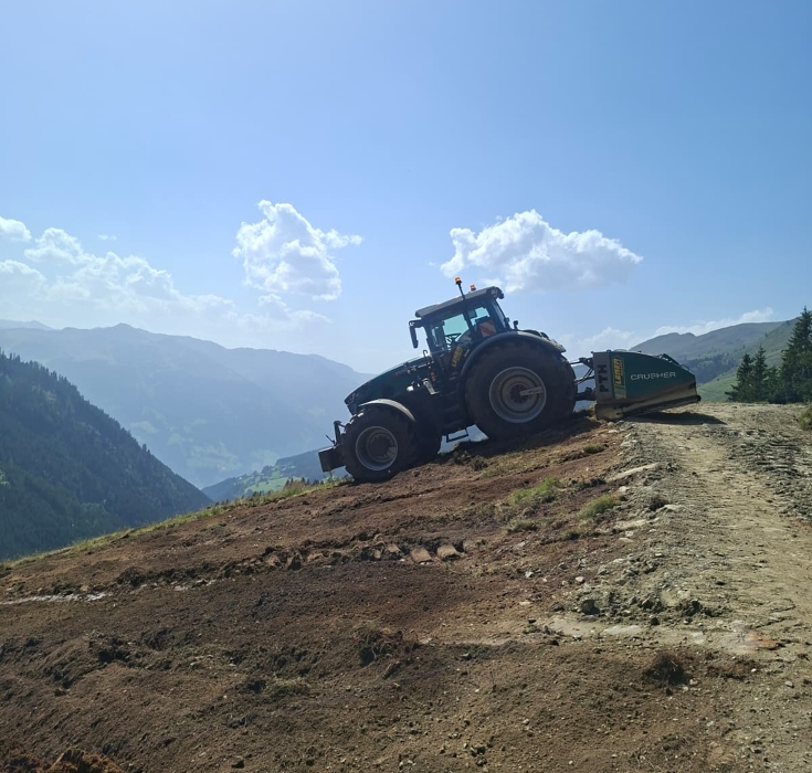 Fendt 942 Varioauf einem steilen Bergweg in den Tiroler Alpen. Der Großtraktor wird für Wegbau, Wegsanierung und Bodenstabilisierung im alpinen Gelände eingesetzt.