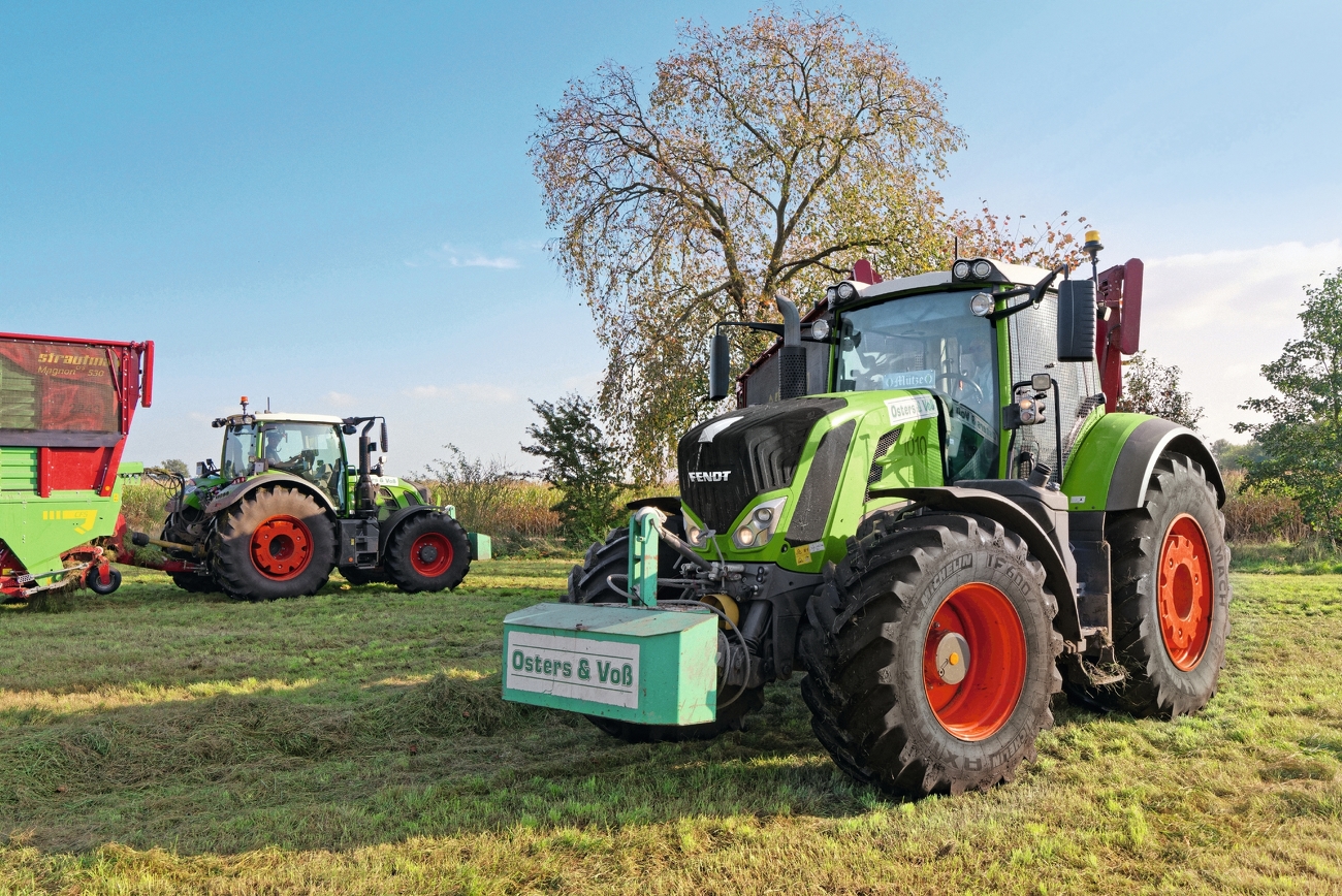 Two Fendt Vario are standing in a meadow. The Fendt Vario on the left is equipped with a loader. The Fendt tractor on the right in the foreground also bears the logo of the contracting company Osters und Voss.