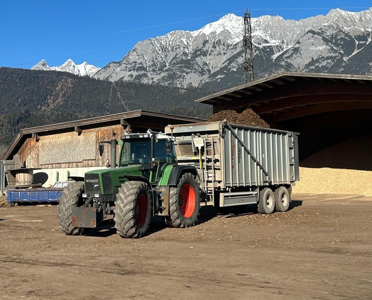 Fendt Favorit 926 Vario with a transport trailer in operation at Lener Hackgut GmbH, set against the impressive mountain scenery of the Tyrolean Alps.
