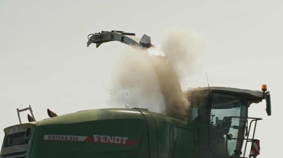 La moitié de la Fendt Katana 850 verte est représentée avec un nuage de poussière et un ciel gris en arrière-plan.