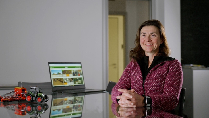Elisa Gregorat est assise à une table. En arrière-plan, on peut voir un ordinateur portable et un petit tracteur- Fendt en jouet.