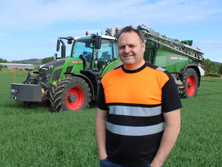 Matthew Mackay se tient dans un champ ; à l'arrière-plan, on aperçoit un Fendt 620 Vario vert aux jantes rouges, traîné par un Rogator.