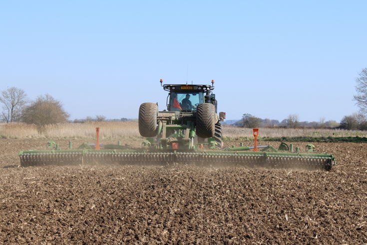 Baksiden av en Fendt 1167 Vario MT som trekker en grønn såmaskin over et jorde, med blå himmel i bakgrunnen.